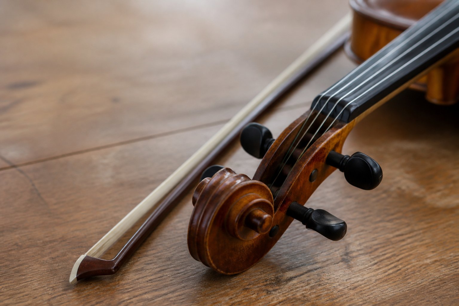 The carved scroll and pegbox of a fiddle lying beside a bow on a bare wooden table